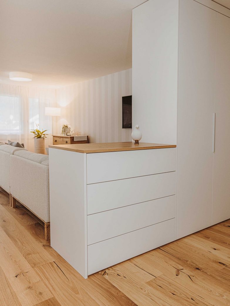 Ein Raumtrenner-Garderobenschrank und eine anschliessende Kommode, die mit dem Eichenparkett harmoniert, zeigen die Vielseitigkeit der individuell angepassten Einbauschränke, auf deren Fertigung das Schweizer Unternehmen seit 58 Jahren spezialisiert ist. ALPNACHNORM.CH