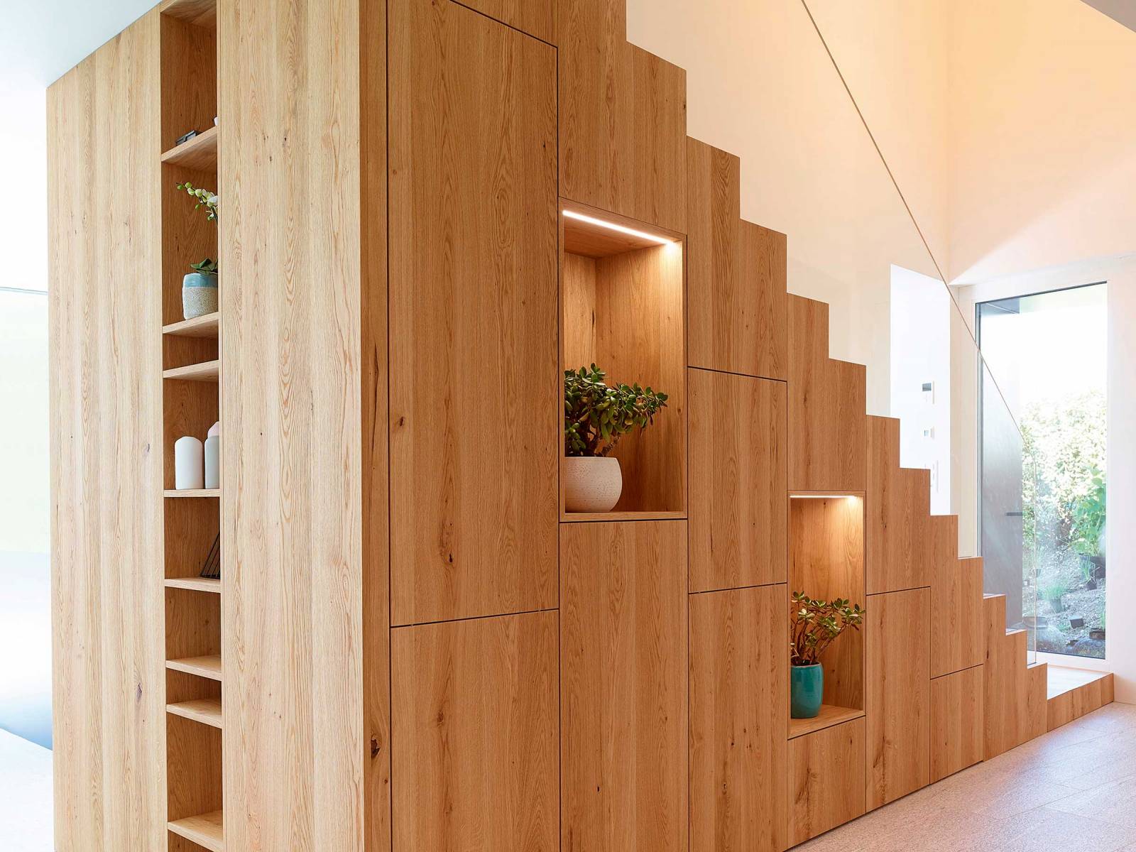 Als führender Spezialist im Bereich Stauraumlösungen ist das Unternehmen der richtige Partner für Speziallösungen wie zum Beispiel dieses grosszügige Treppenelement, das als Raumtrenner, Stauraum und gleichzeitig Regal fungiert. Es beinhaltet Garderobe, Schuh- schränke und Regalflächen für Pflanzen oder Accessoires und wurde zudem mit clever gesetzten Lichtakzenten ergänzt. Alpnach Schränke AG.