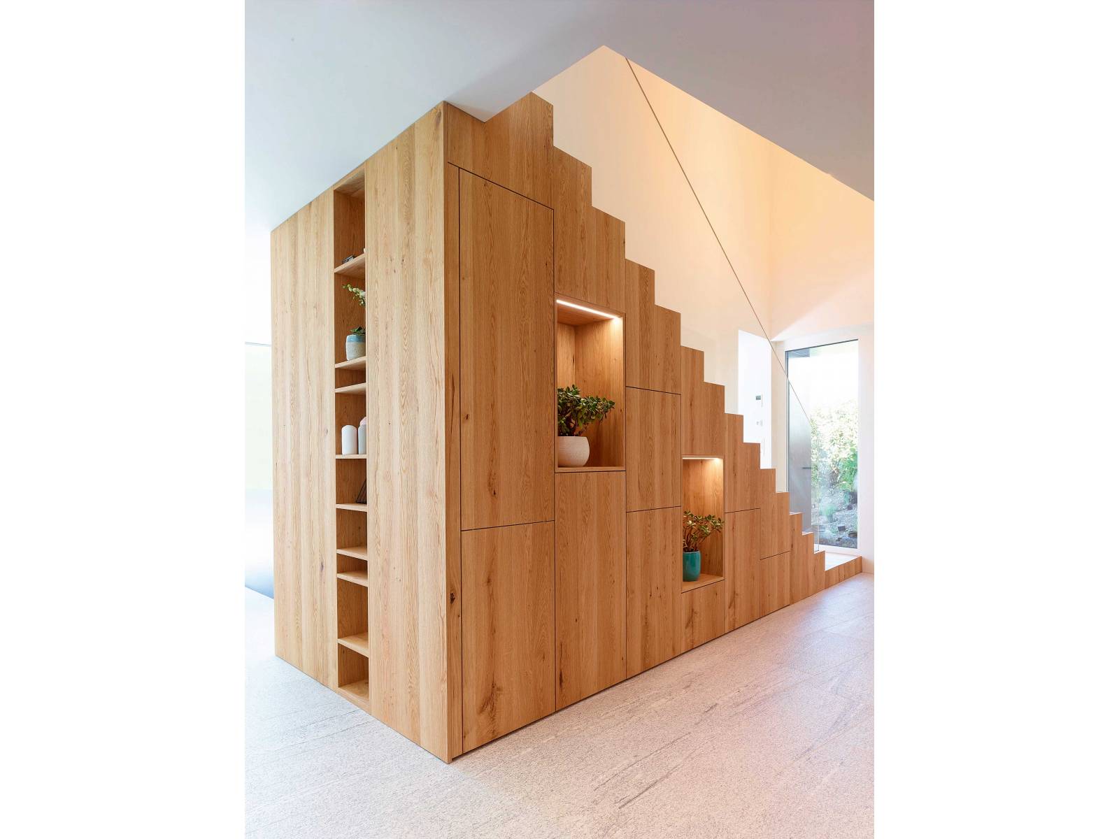 Als führender Spezialist im Bereich Stauraumlösungen ist das Unternehmen der richtige Partner für Speziallösungen wie zum Beispiel dieses grosszügige Treppenelement, das als Raumtrenner, Stauraum und gleichzeitig Regal fungiert. Es beinhaltet Garderobe, Schuh- schränke und Regalflächen für Pflanzen oder Accessoires und wurde zudem mit clever gesetzten Lichtakzenten ergänzt. Alpnach Schränke AG.