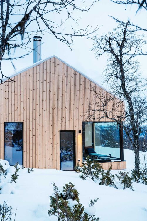 Die Hütte wurde mit Kiefernholz verkleidet, auch das Dach. Sie ist eingeschossig, hat aber genug Deckenhöhe für einen Dachboden, auf dem man aufrecht stehen kann. Die grosszügigen Fenster lassen viel Tageslicht ins Haus. Die Sonne bewegt sich mit den Bewohnern: Sie geht morgens in der Küche auf und später im Wohnzimmer unter.