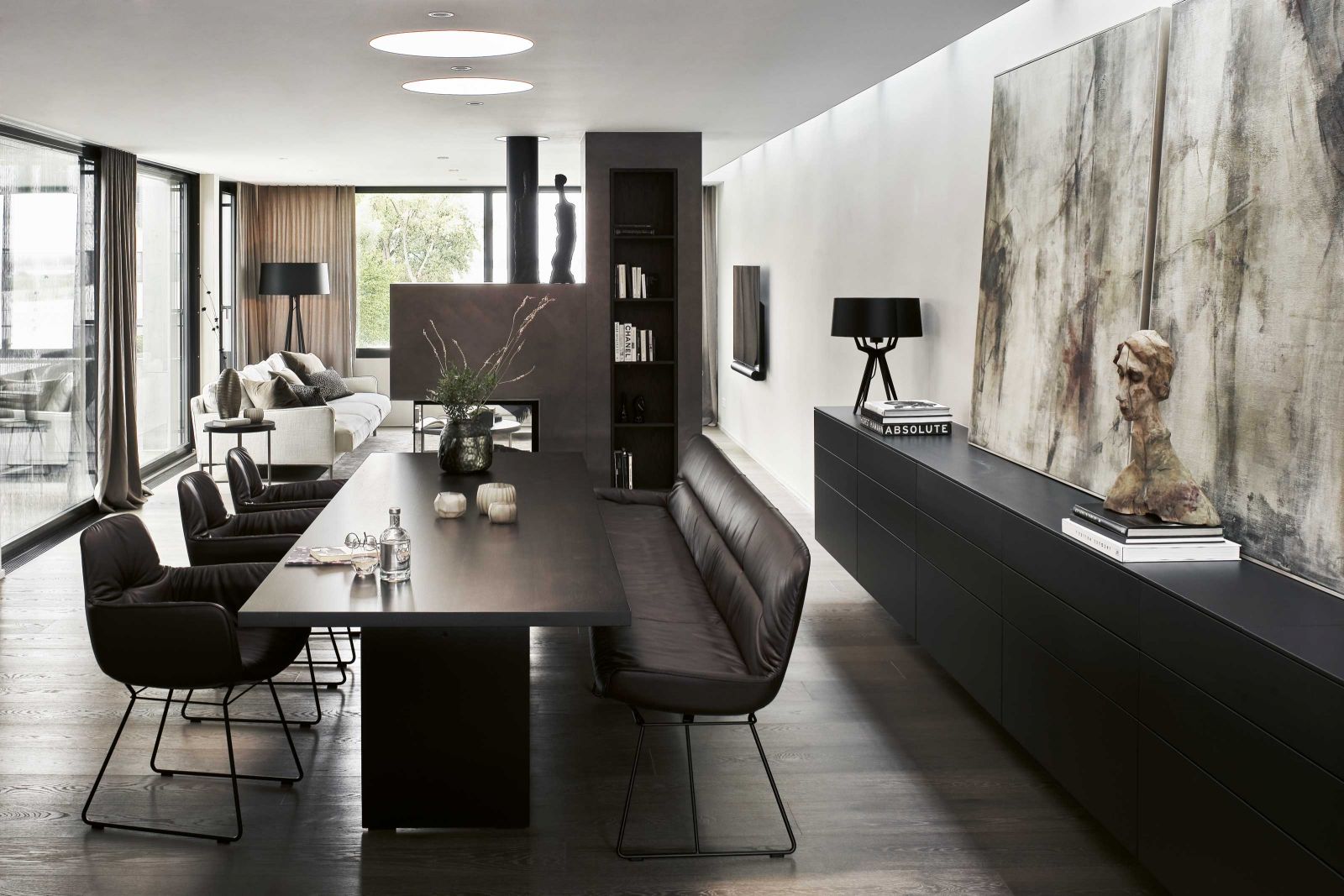 Ein schmales Lichtband über dem Sideboard sorgt für eine gleichmässige Helligkeit. Das Gemälde schuf Daniela Vincenz. In einer Linie mit dem Cheminée steht der Esstisch, Janua. Ledersessel und -bank «Leya» sind von Freifrau.