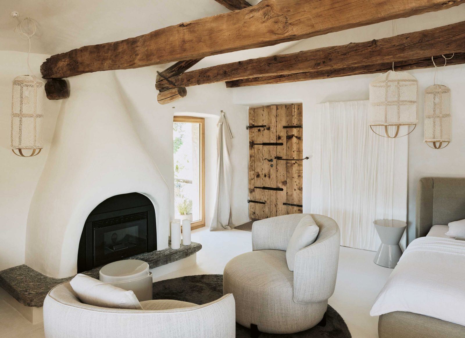 Rund 45 Quadratmeter beträgt die Fläche des Hideaways, auf der Küche, Wohn- und Schlafeinheit sowie ein separates Bad geschickt untergebracht sind. Die alte Holzeingangstüre wurde komplett aufgefrischt. Vor dem Kamin: Sessel «Jane» und Beistelltisch «Lot Stool» von Piet Boon. Bett «Basket» von Bonaldo, Beistelltisch neben Bett: «Cesar» von Minotti.